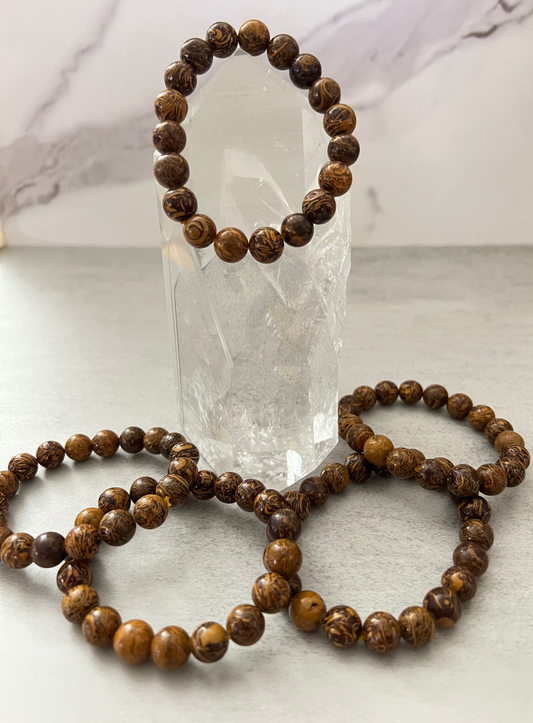 Three brown beaded bracelets on a white surface with a crystal in the background