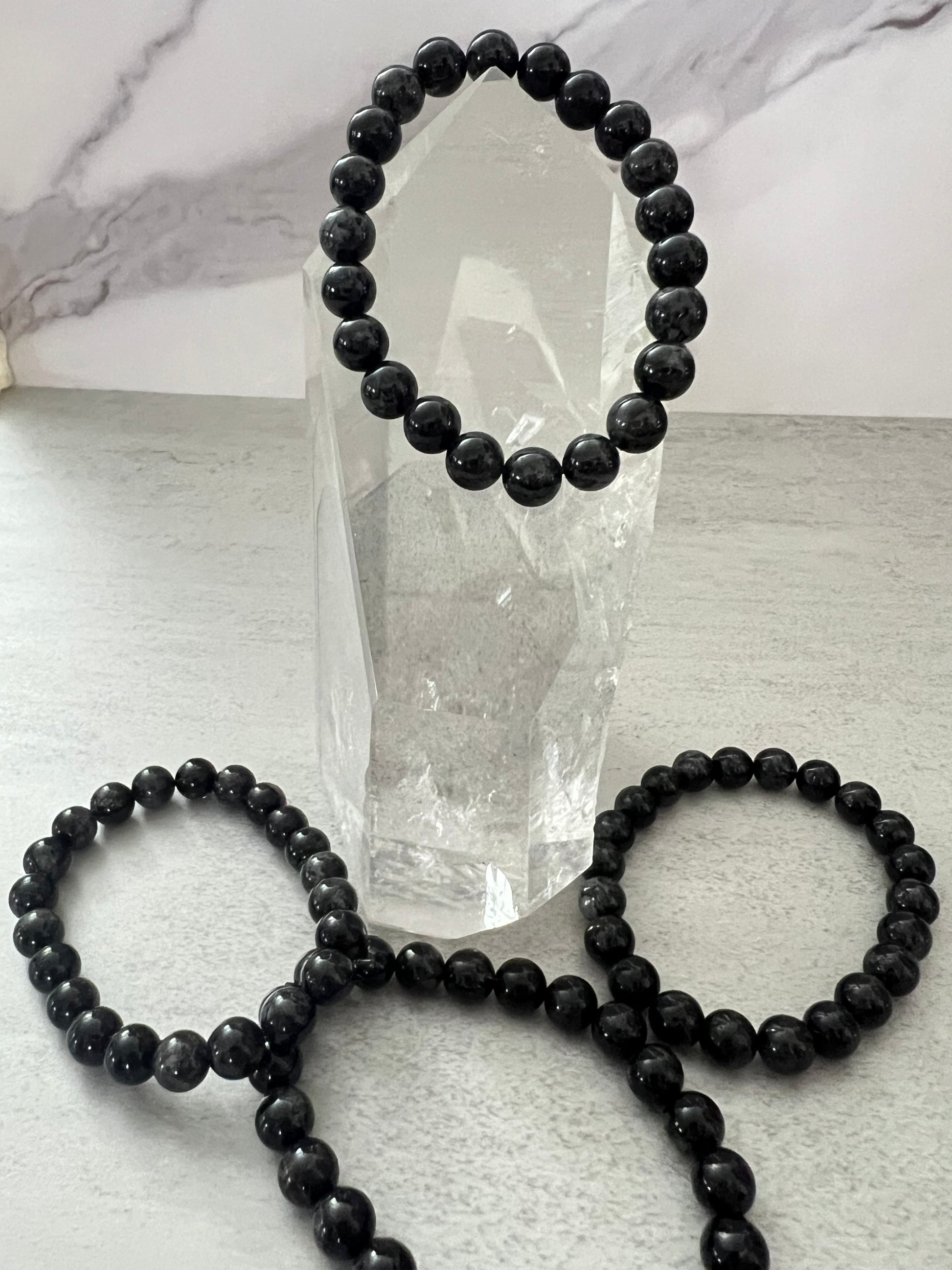 Black beaded bracelets on a light gray surface with a crystal in the background