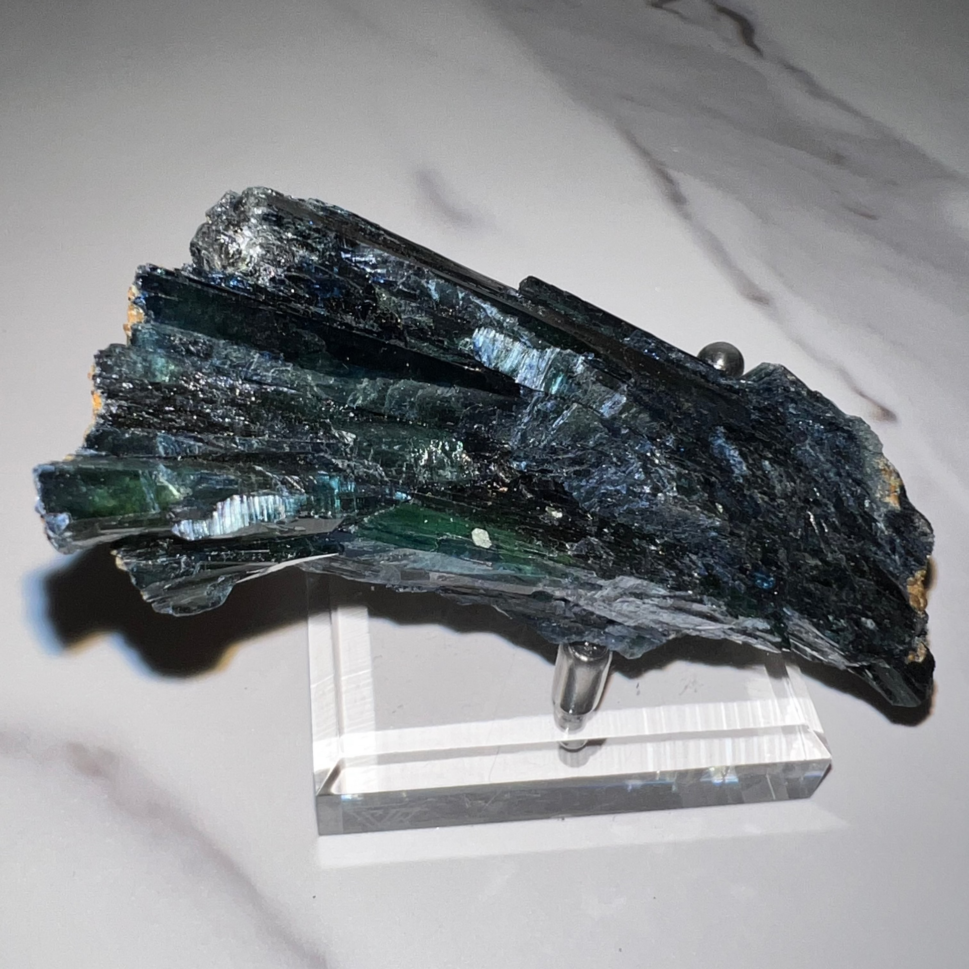 Green mineral specimen on a white stand against a marble background